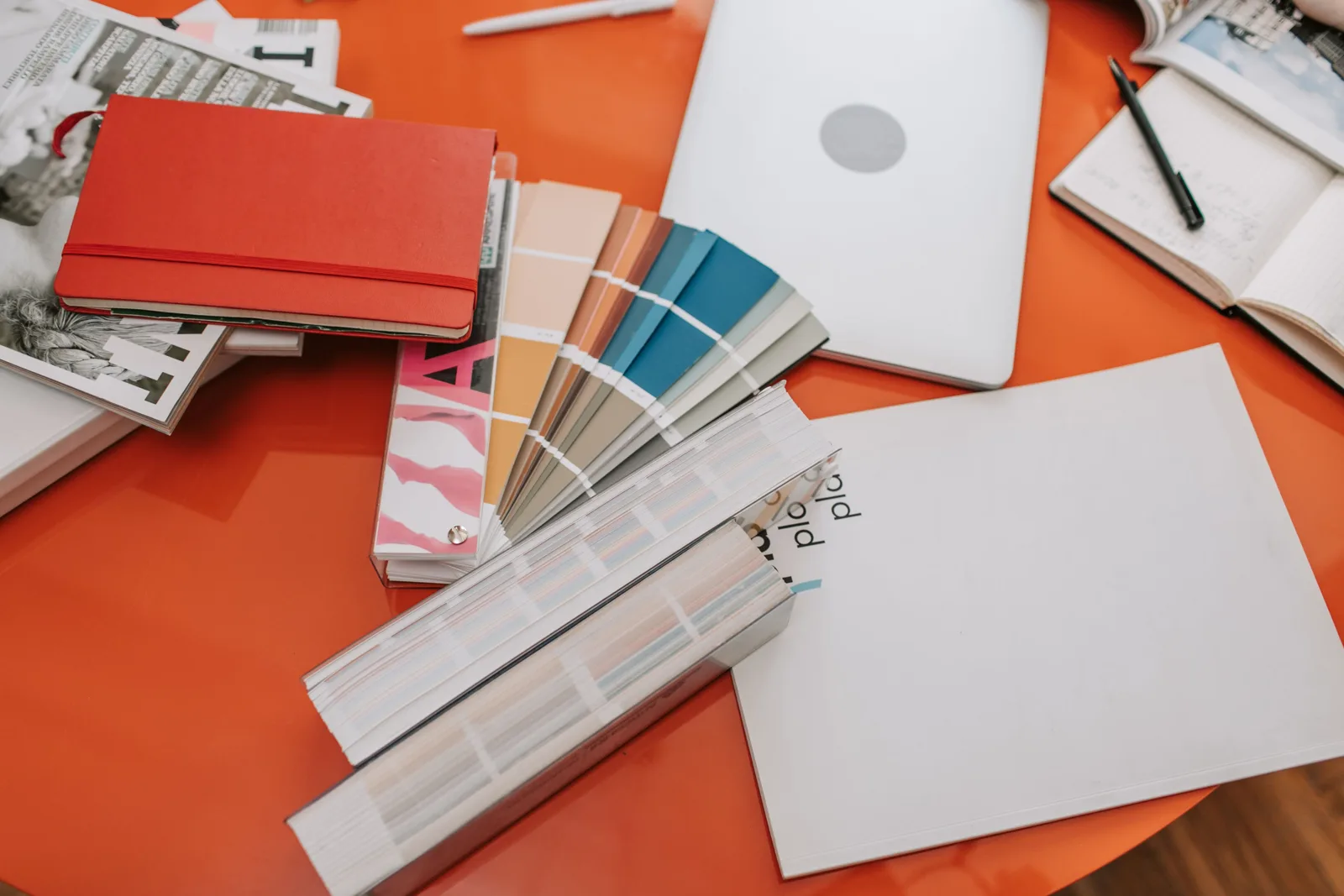 Colour swatches, design books and a laptop spread across an orange creative workspace